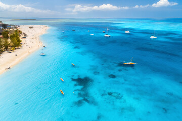 Aerial view of the fishing boats on tropical sea coast with sandy beach at sunrise. Summer holiday in Zanzibar, Africa. Landscape with boat, yacht, clear blue water, green palm trees. View from above