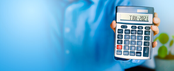 Calculator with Tax word and 202. in woman hand showing number on calculator. Holding to count income and outcome. Business and tax concept. Pay tax in 2021 years. Banner concept. 