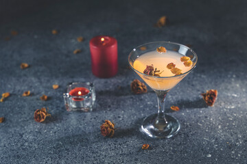 Overhead view of grapefruit martini cocktail with dried roses flowers and petals, surrounded candles on dark gray table surface.