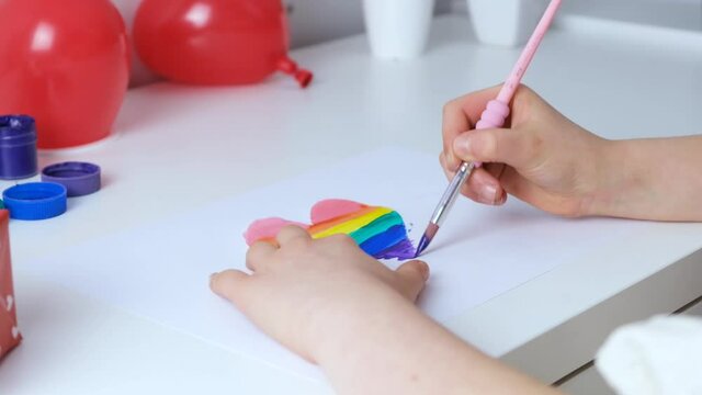 Close-up girl paints the heart in rainbow colors. Love symbol. Slow motions