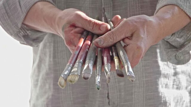 Close-up of midle aged spanish artist holding  paintbrushes with hands covered in paint.