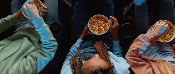 Top view of friends holding baskets of popcorn while watching movie together at the cinema