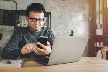 Asian businessman using mobile phone with laptop for work from home in house when covid-19 pandemic, technology 5G is coming, business and wireless after coronavirus outbreak new normal life style.