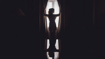 Cute young woman bride in home bathrobe at window in hotel room. Morning of bride on wedding day. Happy female is waiting to meet her groom. Concept of happy and luxury married. Copy space