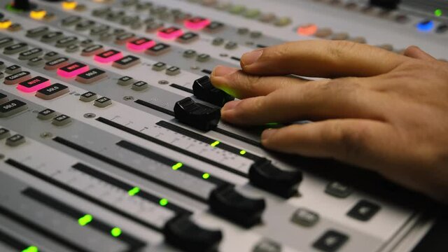 Sound engineer is moving levers of a multitrack mixing console in the control room during a recording session