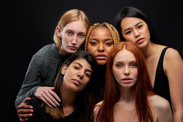 mixed race group of ladies isolated on black background, young women of different ethnicity seriously looking at camera