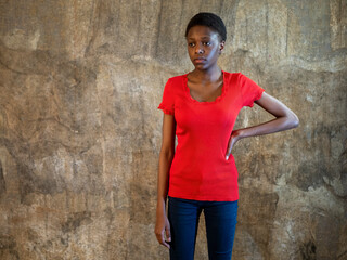 Naklejka na ściany i meble African american woman in red bodysuit and jeans stands against wall in studio posing for camera