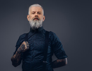 Trendy and confident grandfather with tattooed hands dressed in modern clothing poses in dark background.