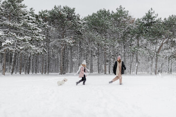 mother and daughter walk in winter forest with dog