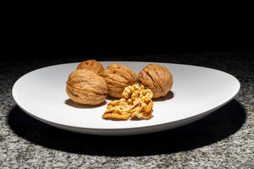 Walnuts in a shell on a white plate and dark background