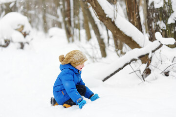 Fototapeta na wymiar Little boy having fun playing with fresh snow. Active outdoors leisure for child in snowy winter day.