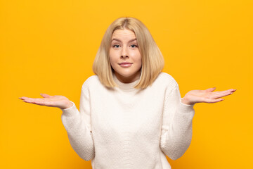 blonde woman feeling puzzled and confused, doubting, weighting or choosing different options with...