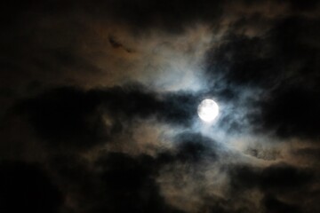 Naklejka na ściany i meble The full moon hiding in the cloudy night sky. Dark background of the moonlight and clouds