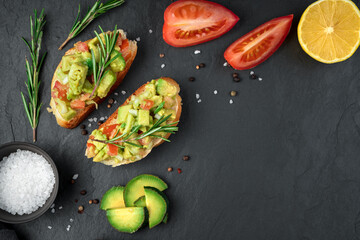 Two toasts with guacamole, tomatoes, lemon, rosemary and spices on a black background. Top view, with space to copy. The concept of healthy eating.