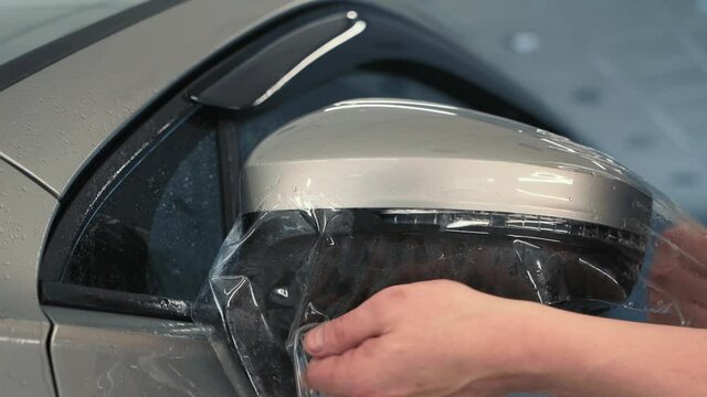 Workers hands wraps wet Paint Protection Film or anti-gravel protection coating on car mirror. Car detailing.