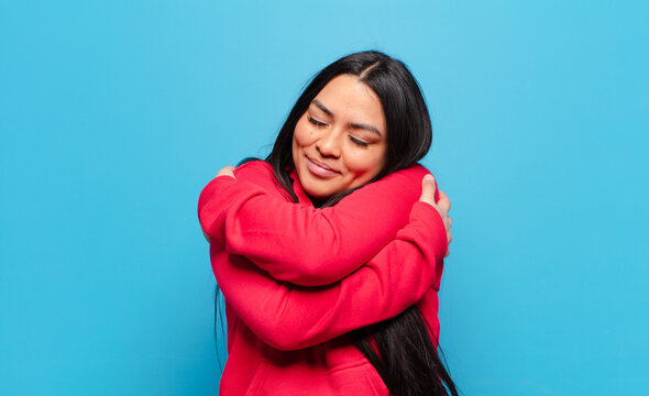 latin woman feeling in love, smiling, cuddling and hugging self, staying single, being selfish and egocentric