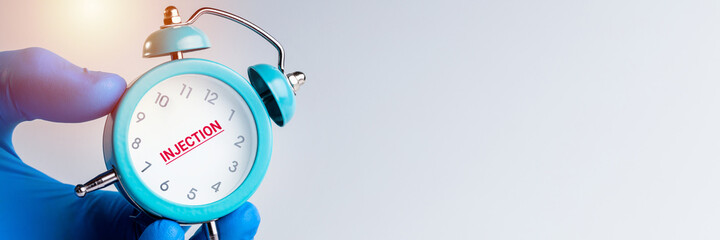 medical worker holding alarm clock over gray background. time to injection concept. medicine conceptual