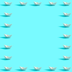 Pattern on a blue background and white paper boats anarranged as frame with copy space. Symbol of summer and travel.