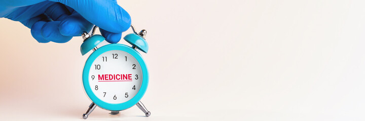 medical person holding alarm clock over grey background. word medicine on clock face. copy space....