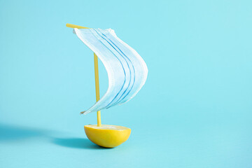 a creative concept of a sailboat made of medical mask and lemon on a blue background. A symbol of health care.