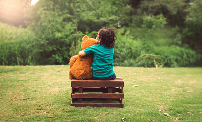 Niño sentado sobre caja de madera abrazando oso de peluche en el campo © Brandon