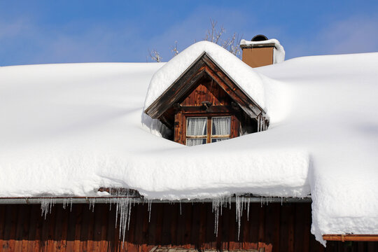 Eine Dachfenster mit viel Schnee und Eiszapfen von einem alten Bauernhaus in Bayern