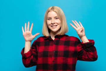 blonde woman smiling and looking friendly, showing number nine or ninth with hand forward, counting...