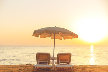 Beige cotton beach umbrella with two sunbeds by the sea