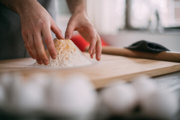 A male chef prepares noodle dough at home in the kitchen. Close up of hands with flour and dough
