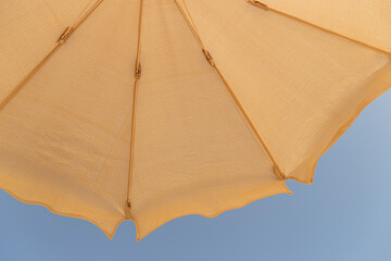 Beige cotton beach umbrella against a blue sky