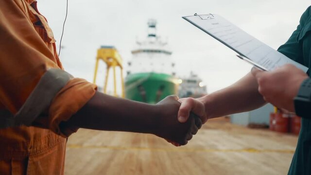 marine contractor businessman handshaking with worker on the ship with contract agreement. Handshake of two boilersuits with different colors wiyh maritime background