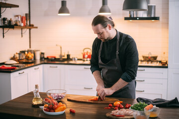 A male cook prepares vegetables at home in the kitchen