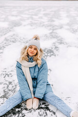 Fototapeta na wymiar Young blonde woman, sitting on ice on frozen lake, on a cold winter day.