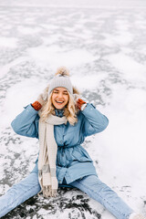 Fototapeta na wymiar Cheerful young woman with big smile, sitting on ice on frozen lake, on a cold winter day.