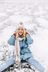 Fototapeta na wymiar Happy young woman, sitting on ice on frozen lake, on a cold winter day, smiling.