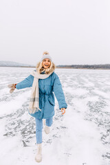 Cheerful blonde woman running on ice on a frozen lake on a cold winter day.