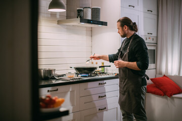 A male cook is cooking at the stove at home in the kitchen