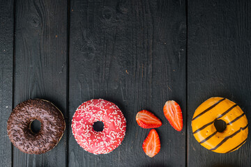 Glazed donuts, on black wooden table background, top view flat lay with copy space for text