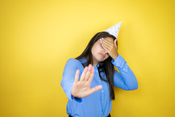 Young caucasian woman wearing a birthday hat over isolated yellow background covering eyes with hands and doing stop gesture with sad and fear expression. Embarrassed and negative concept.