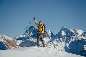 A climber on the top of a mountain stands with a raised hand
