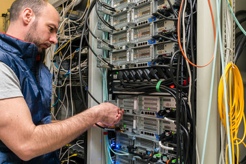 The man serves the server hardware. A technician switches internet wires in a server room. The...