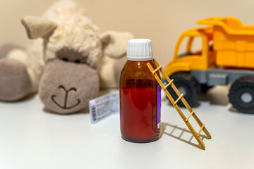 small wooden ladder. prescription and medicine syrup. open bottle. with children toys in background. small wooden ladder.