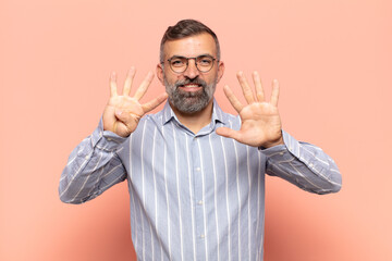 adult handsome man smiling and looking friendly, showing number nine or ninth with hand forward,...