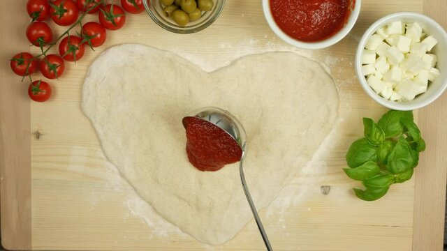 Heart shaped pizza making put tomato sauce on pizza, love Italian pizza