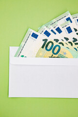 Euro banknotes in a white envelope on green background. 