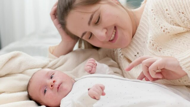 Portrait of adorable newborn baby and happy smiling mother. Mom tickling and playing with child in crib. Concept of family happiness and loving parents with little children