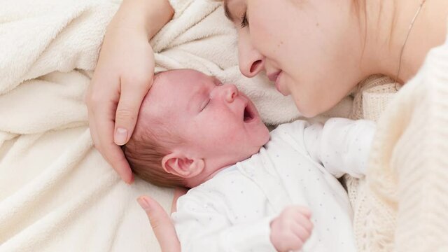 Closeup shot of little newborn baby lying next to mother and crying. Happy smiling woman looking at her little child. Concept of family happiness and loving parents with little children