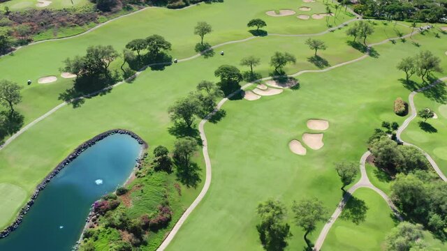 Golf club establishing shot. Green golf course background. Aerial view on blue lake on perflect green lawn with trees and sand pools. People using carts to drive by the field to play the prestige game