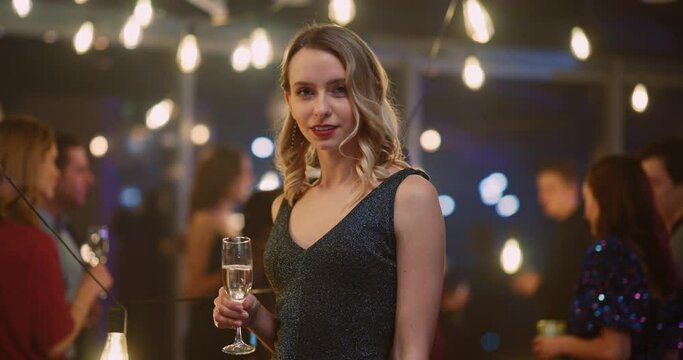 Beautiful Blonde Young Sexy WOman in Elegant Outfit Drinking Glass of Wine Smiling to Camera Celebrating Holiday at the Company. Corporate Party.