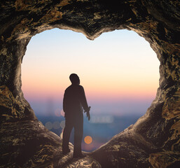 Worship God concept: Silhouette human standing on cave of heart against blurred mountain sunrise...